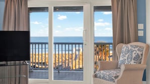 Ein Balkon mit Blick auf Strand und Meer, ein Korbstuhl und ein Fernseher auf einem Tisch.