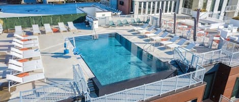A rooftop pool with sun loungers and a view of the cityscape.