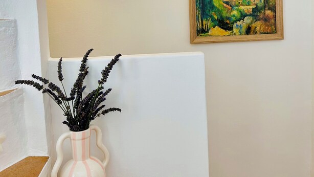 A room with a white wall, a painting of a landscape, a vase with lavender, and a wall-mounted light fixture. - Charming house in the center of Aix, quiet, absolute, bright. (Aix-en-Provence)