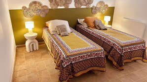 A room with two beds, each with patterned bedding, a wall-mounted decorative piece, and a bedside lamp. - Charming house in the center of Aix, quiet, absolute, bright. (Aix-en-Provence)