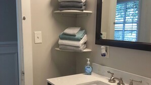 A bathroom with a white sink, dark cabinets, a mirror, and shelves with folded towels.