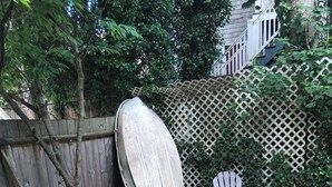 A backyard with a wooden deck, a metal table, and two Adirondack chairs.