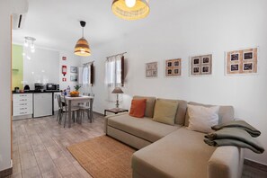 A modern living room with a sofa, a dining table, and a kitchen in the background.