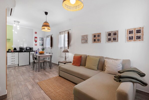 A modern living room with a sofa, a dining table, and a kitchen in the background.
