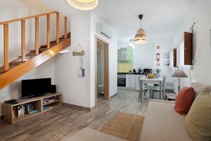 A modern living room with a wooden staircase, a flat-screen TV, a sofa, and a kitchen area in the background.