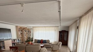 Een ruime woonkamer met een zithoek, een eettafel met stoelen en een boekenkast.
