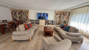 Een ruime woonkamer met een grote flatscreen televisie, twee banken, een salontafel en een eethoek met een houten tafel en stoelen.