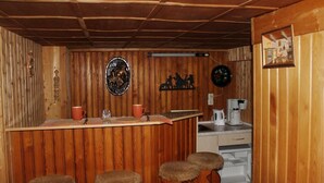 Un intérieur en bois comprenant un bar, des tabourets, une machine à café et un réfrigérateur.