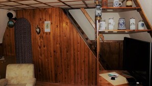 Une pièce aux murs en bois, avec un escalier, une télévision et une étagère remplie de bocaux.