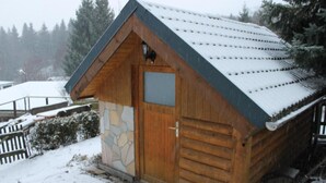 Une cabane en bois avec une façade en pierre, un toit à deux versants et une porte en bois.