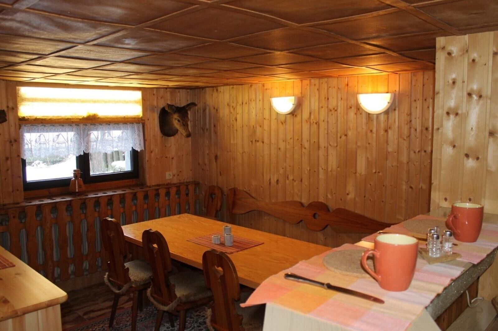 Un intérieur en bois comprenant une table, des chaises, une fenêtre et des lampes fixées au mur.
