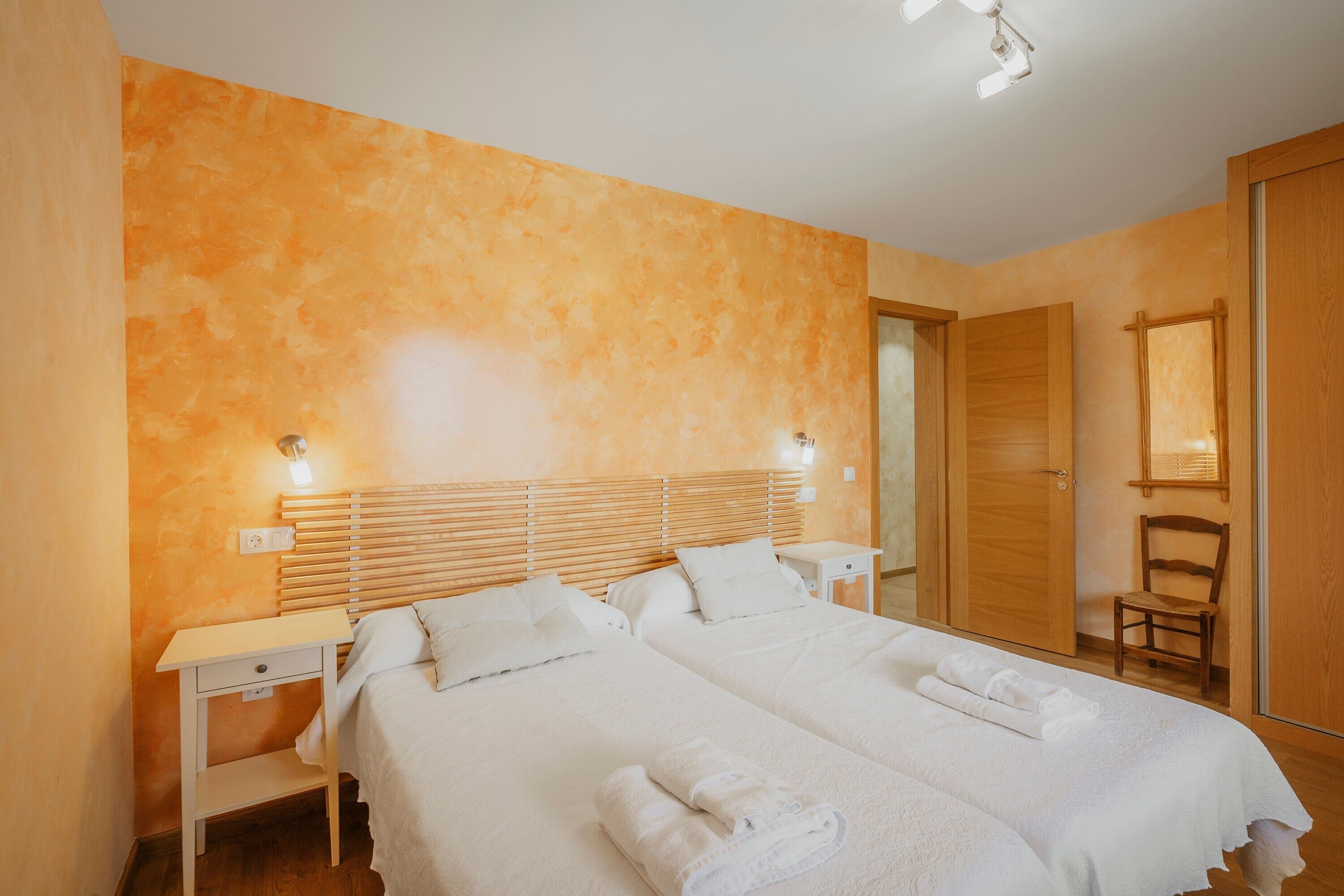 A hotel room with two beds, a wooden headboard, a nightstand, a chair, and a mirror.