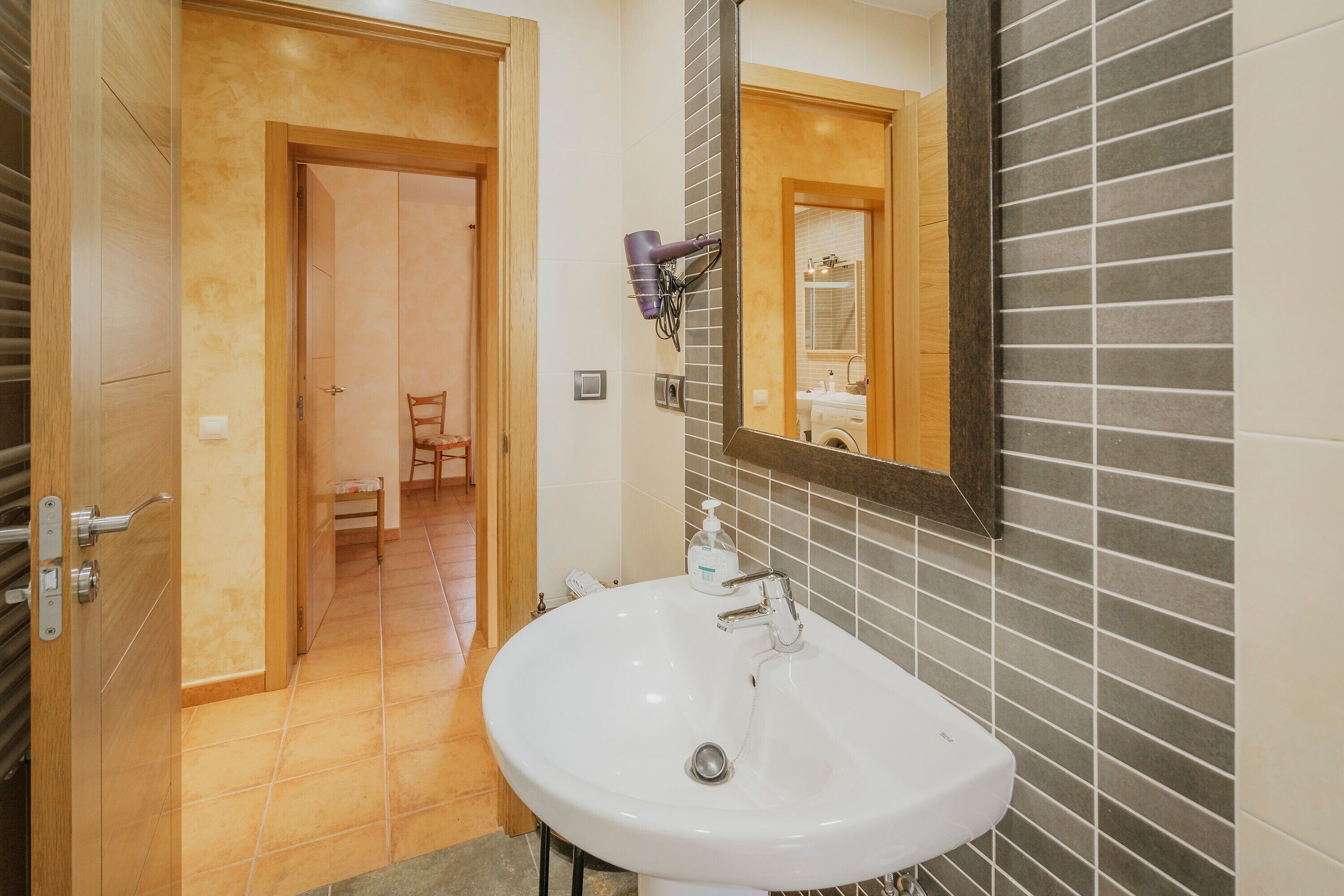 Une salle de bain avec un lavabo blanc, un miroir et un sèche-cheveux fixé au mur.