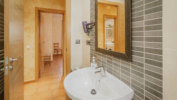 Une salle de bain avec un lavabo blanc, un miroir et un sèche-cheveux fixé au mur.