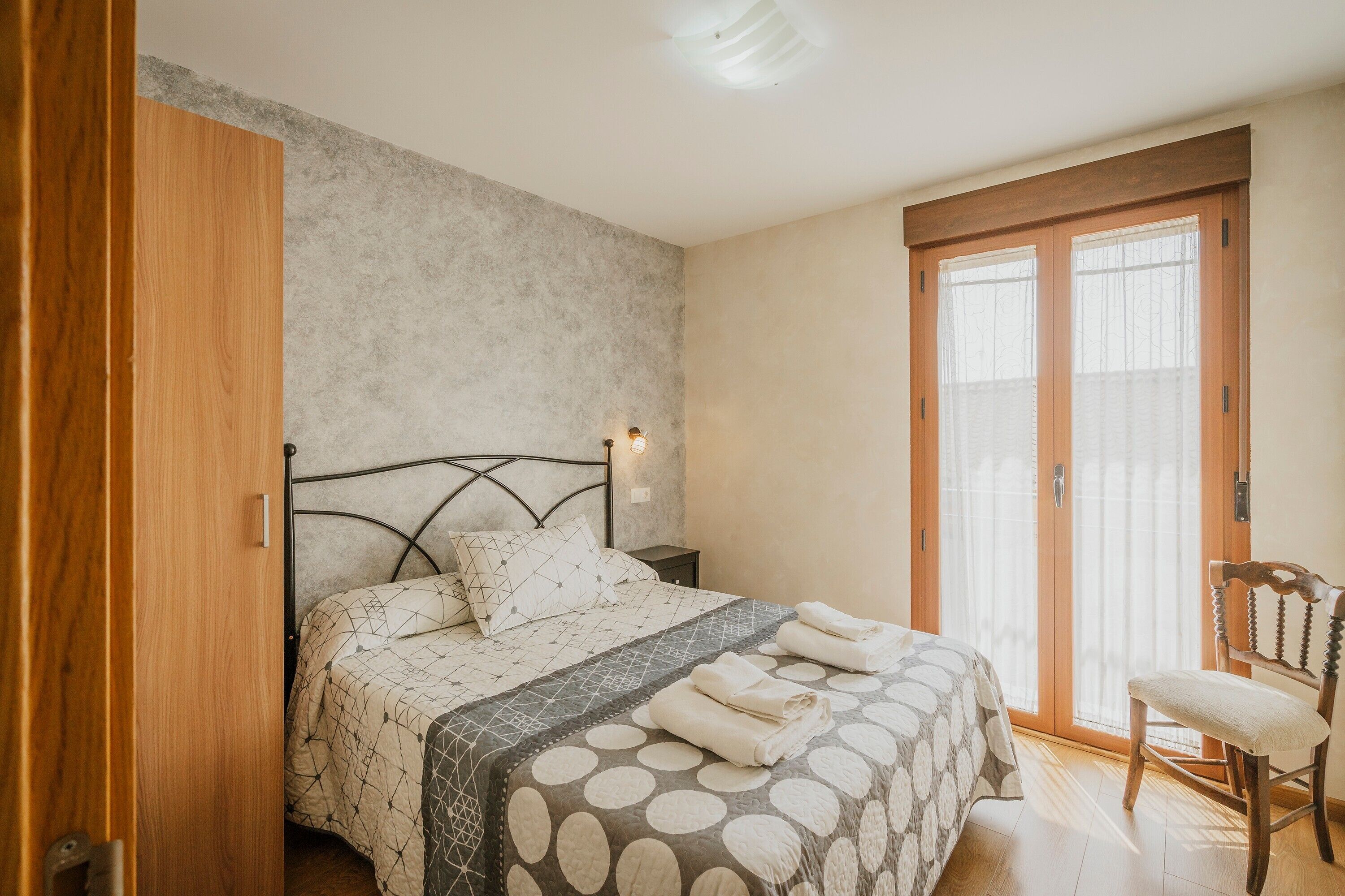 Un dormitorio con cama, una silla, una mesita de noche y un ventanal corredizo.