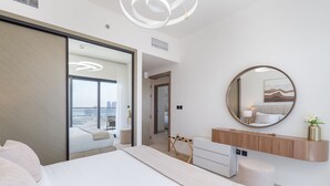 Une chambre d’hôtel moderne avec un grand lit, un miroir rond, une coiffeuse en bois et une vue sur la ville.