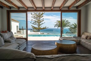 A spacious living room with a large sliding glass door leading to a pool and ocean view. - Villa 'TheCUBE' with Sea Views, Wi-Fi, and Air Conditioning (Tarifa)
