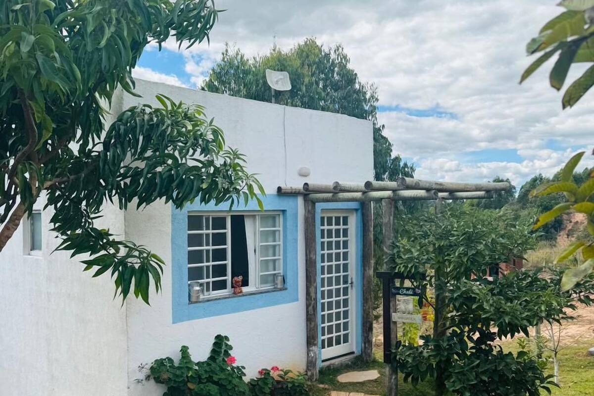 Une petite maison avec une porte et des fenêtres bleues, entourée de verdure et bordée d’un chemin de pierres.