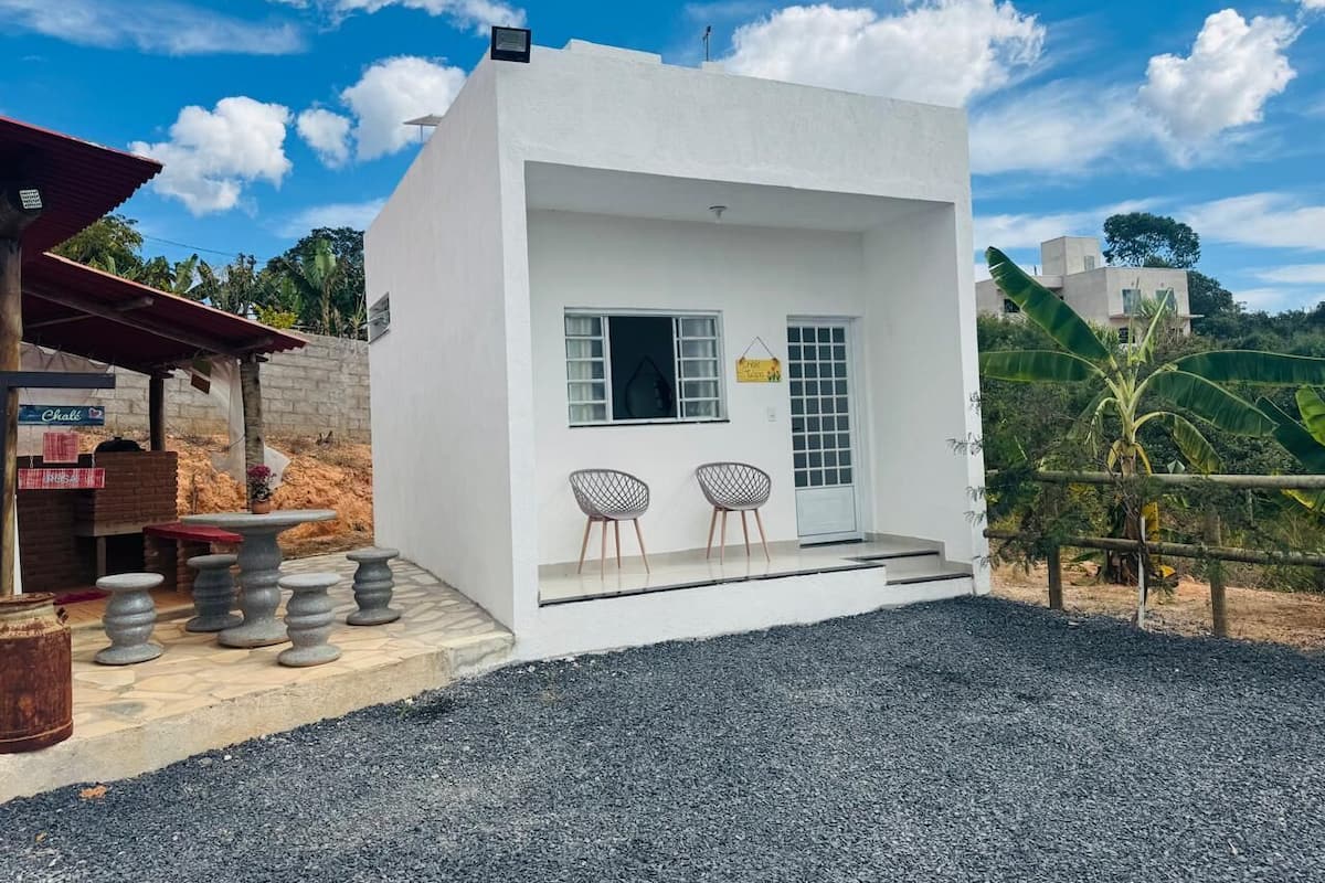 Un petit bâtiment blanc avec une seule porte et une seule fenêtre, deux chaises à l’extérieur et une allée gravillonnée.