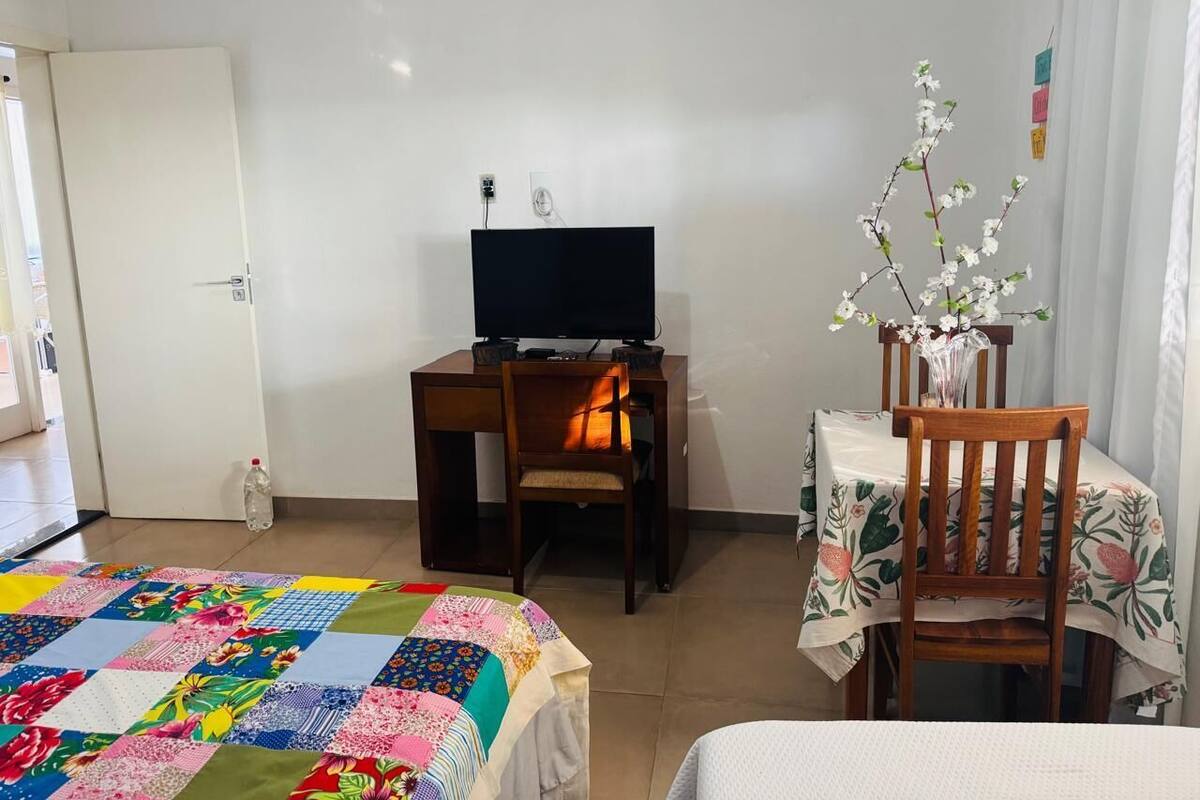 Une chambre d’hôtel avec un lit, un bureau avec un ordinateur, une chaise et une petite table sur laquelle est posé un vase de fleurs.