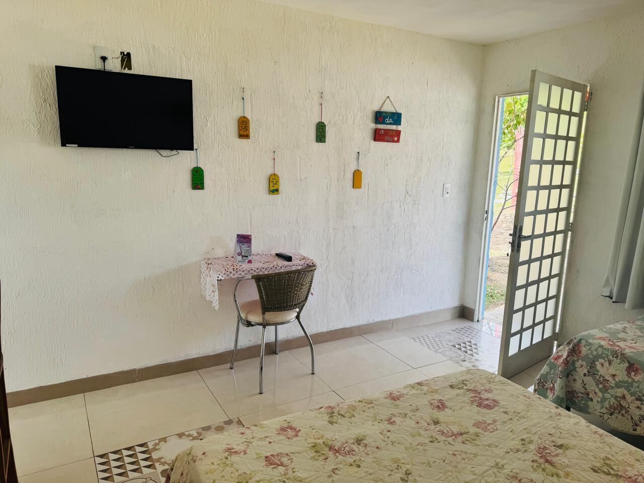Une pièce comprenant un lit, une table avec une chaise, un téléviseur fixé au mur et une porte donnant sur l’extérieur.