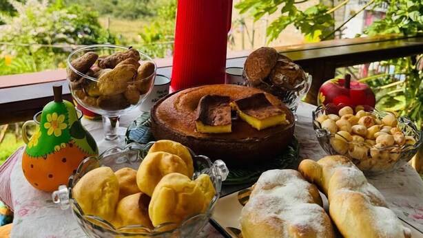A table with various pastries and a red thermos on a balcony overlooking a scenic landscape. - Pousada Dona Terezinha (Formiga)