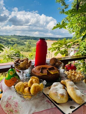 A table with various pastries and a red thermos on a balcony overlooking a scenic landscape. - Pousada Dona Terezinha (Formiga)
