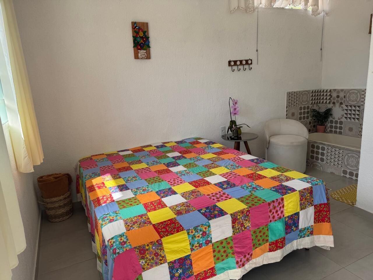 Un dormitorio con un edredón acolchado de colores, una mesita redonda con una lámpara y una silla blanca.