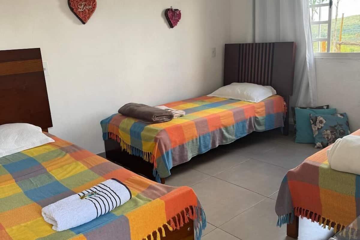 Une chambre avec deux lits, chacun recouvert d’une couette à carreaux colorés et agrémenté d’un oreiller blanc. Les murs sont décorés de motifs en forme de cœur et il y a une fenêtre avec des rideaux.