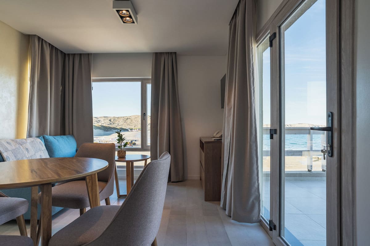 A modern room with a dining table, chairs, a sofa, and a balcony with a view of the sea.