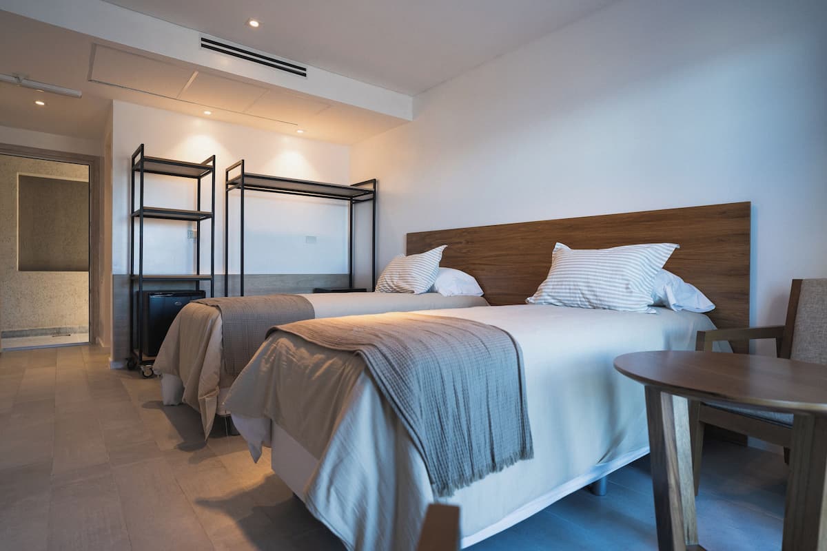 A modern hotel room with two beds, a wooden headboard, a small table, and a TV on a stand.