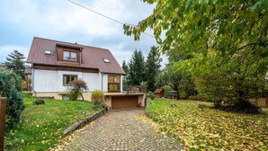 Une maison avec une allée pavée, un garage et un jardin agrémenté d’arbres et de pelouse.