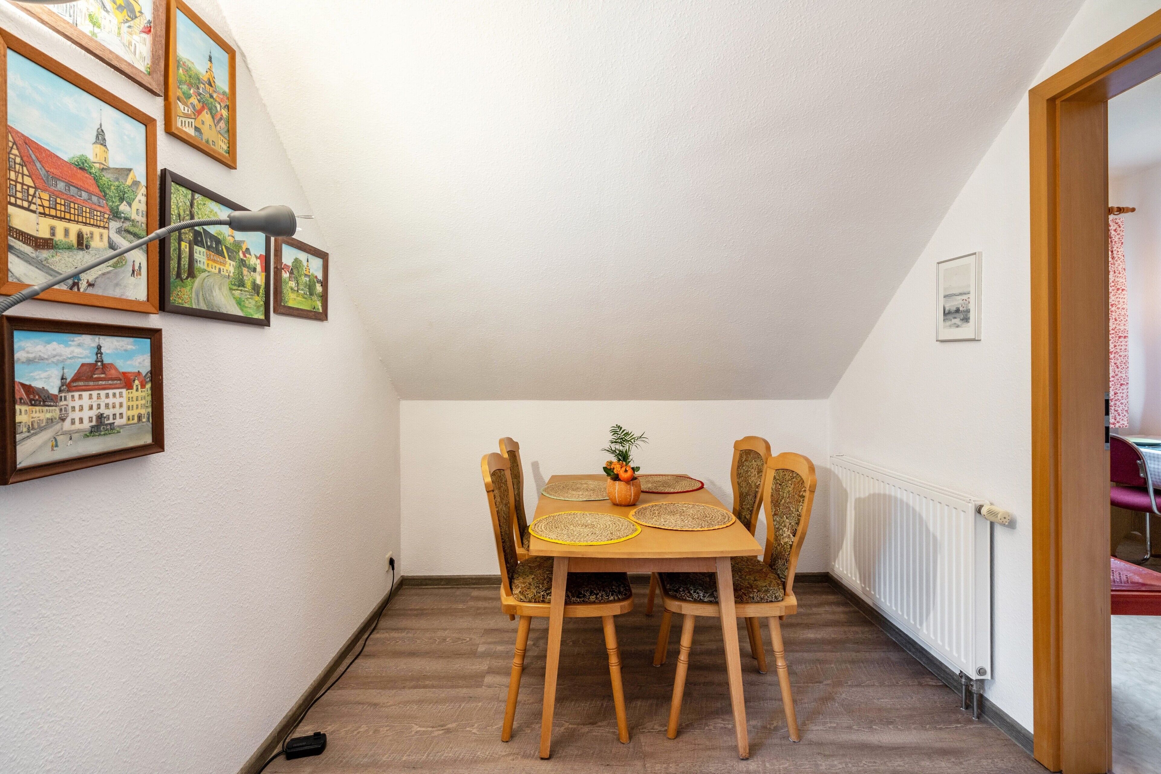 Un coin repas comprenant une table, des chaises, une lampe et des tableaux encadrés accrochés au mur.