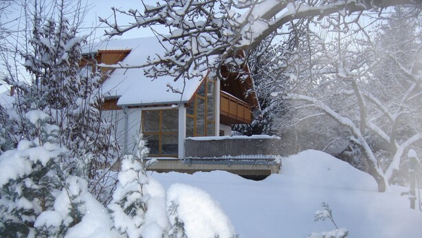 Un bâtiment enneigé, doté de grandes fenêtres et d’un balcon en bois.