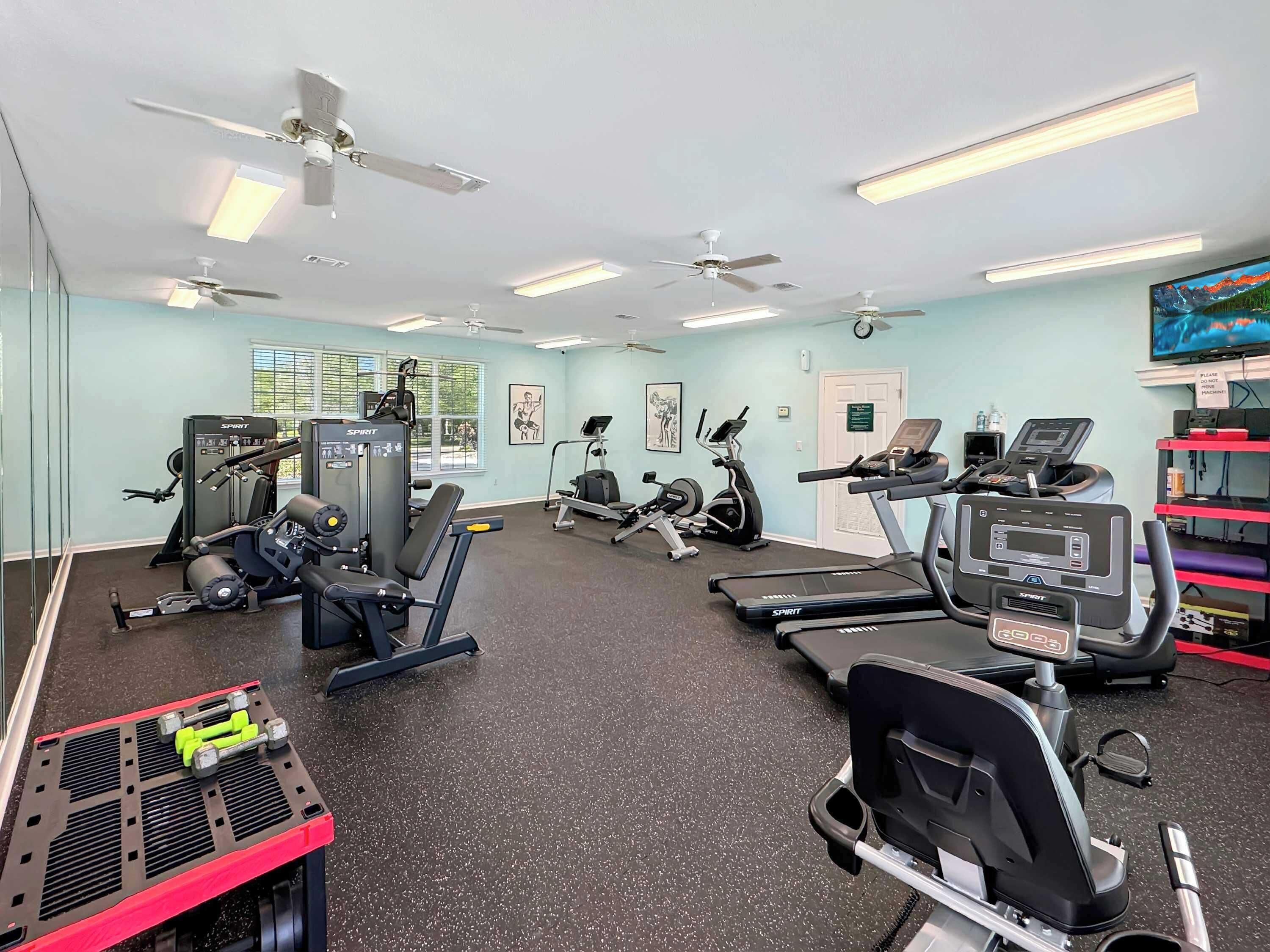Een sportschool met diverse fitnessapparaten, plafondventilatoren en fluorescent verlichting.