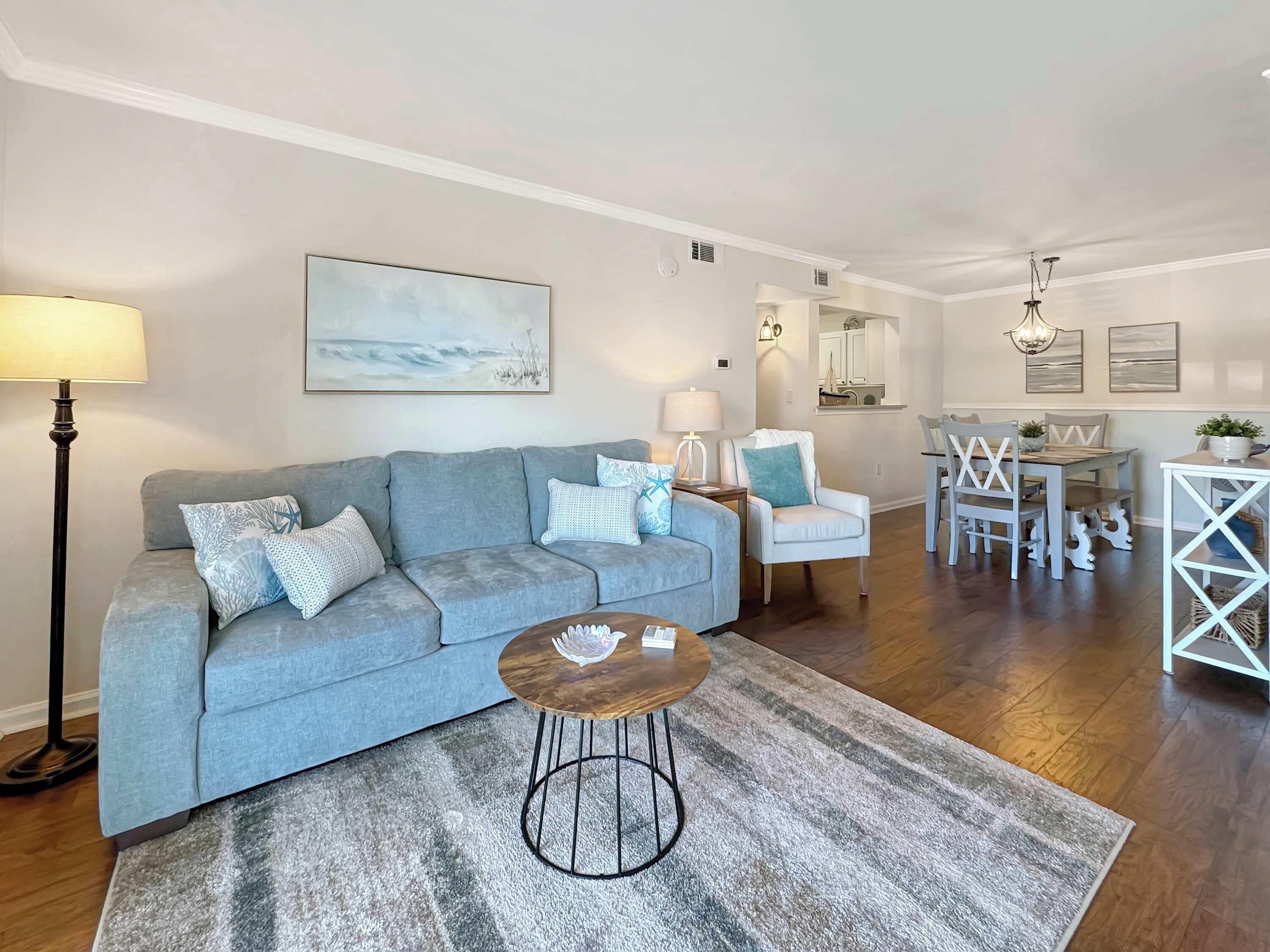 Un salon avec un canapé gris, une table basse ronde et un coin repas comprenant une table et des chaises blanches.