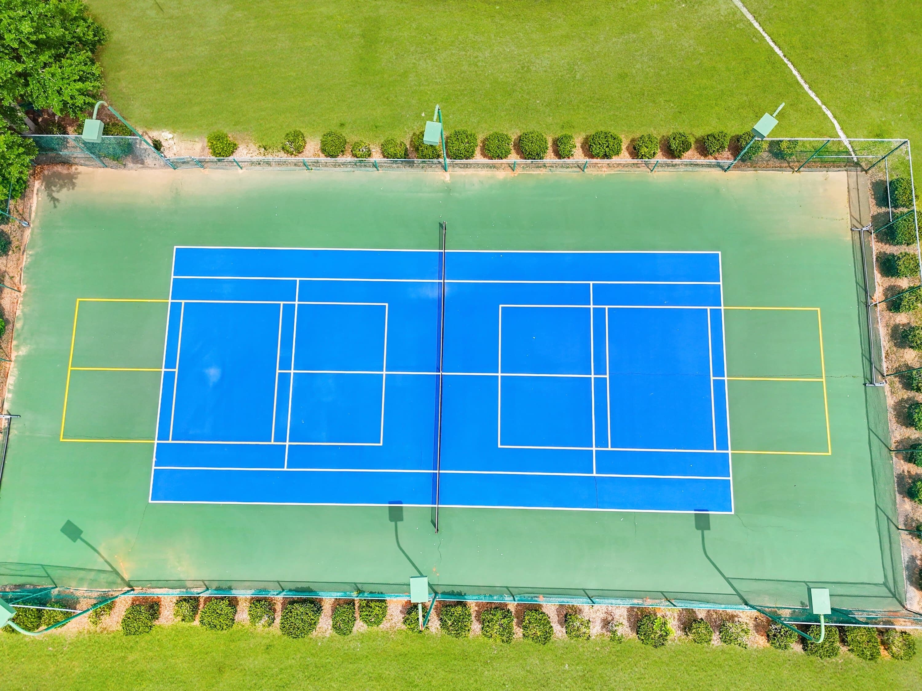 Vista aérea de una cancha de tenis con zonas verdes y una valla.