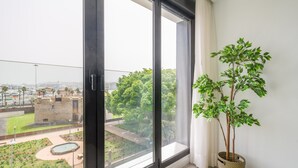 Una stanza con un'ampia finestra, una pianta in vaso e vista su un paesaggio urbano con spazi verdi ed edifici.