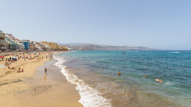 Una spiaggia con acque cristalline, persone che nuotano e si rilassano al sole, e edifici lungo la costa.