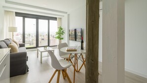 Un soggiorno moderno con una grande finestra, un divano, un tavolo da pranzo con sedie, una TV e una pianta.