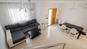 Una sala de estar moderna con un sofá seccional gris, una mesita de centro negra y un comedor con una mesa negra y sillas blancas.