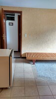Um quarto com piso de azulejos, um banco de madeira, uma escrivaninha e uma porta com uma placa.