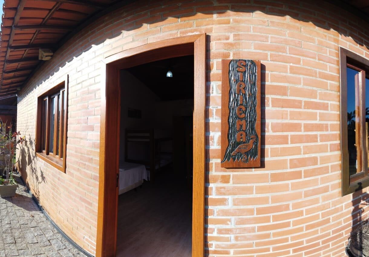 Um edifício de tijolos com fachada curva, porta aberta que dá para um quarto com cama e mesa de cabeceira, e uma placa decorativa com um pássaro.