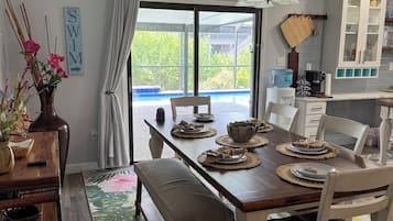 A dining area with a wooden table set for four, a bench, and a view of a swimming pool through large glass doors.