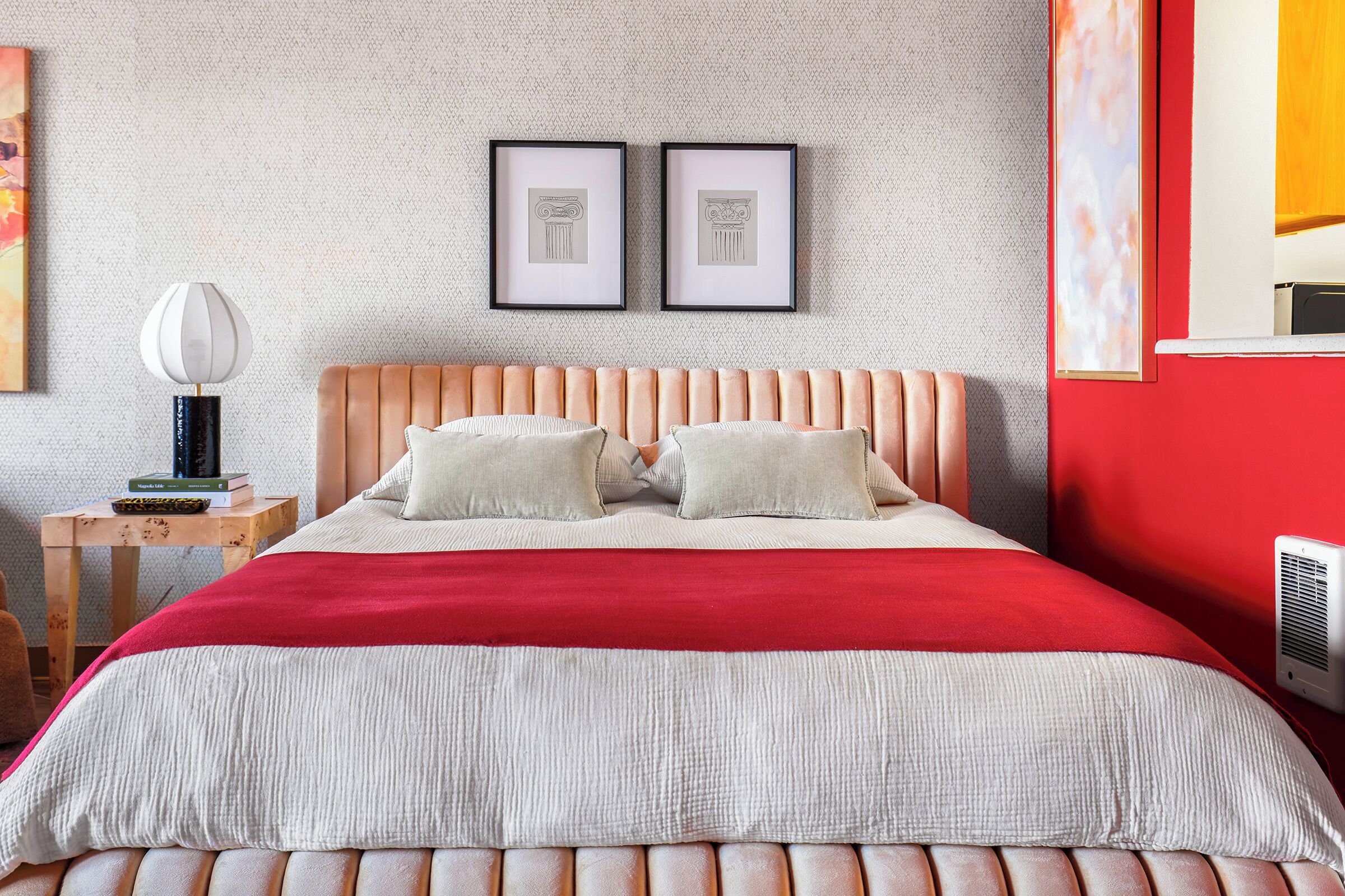 A bedroom with a bed, pillows, a nightstand, a lamp, and framed pictures on the wall.