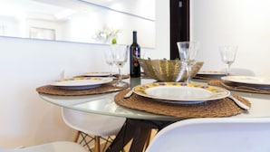 A dining table with a glass top, surrounded by white chairs.