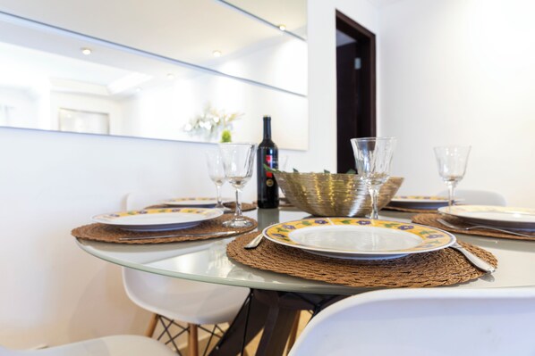Una mesa de comedor con cubierta de vidrio, rodeada de sillas blancas.
