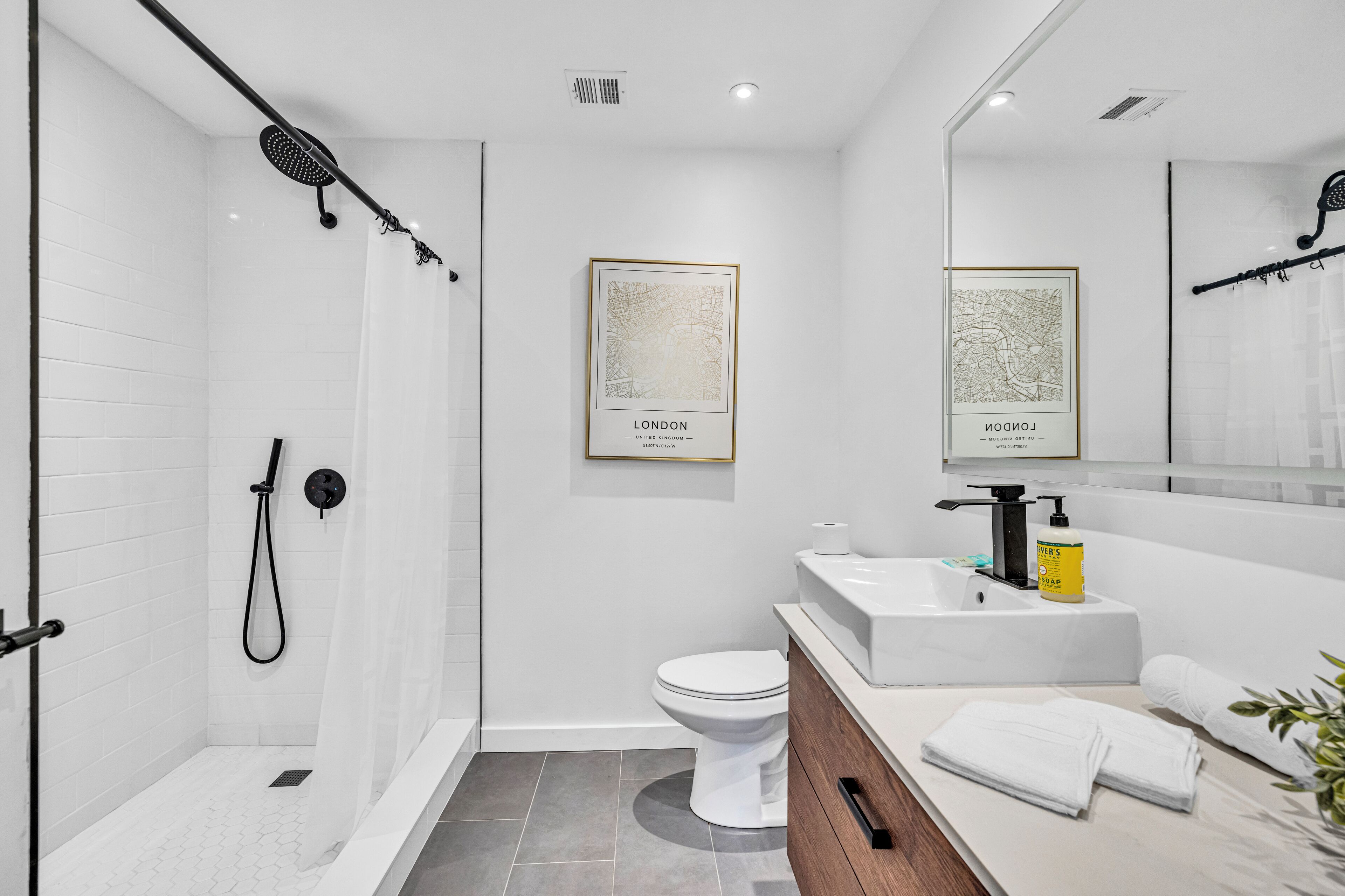 A modern bathroom with a glass-enclosed shower, a toilet, a sink with a mirror, and two framed maps of London.