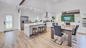 Une cuisine moderne dotée d’un îlot central, de tabourets de bar et d’un coin repas avec une table et des chaises en bois.