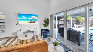 Un salon moderne doté d’un grand téléviseur, de sièges confortables et offrant une vue sur une terrasse extérieure avec une piscine.